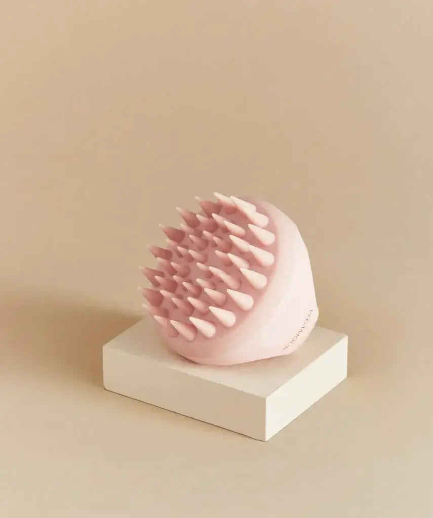 Masseur revitalisant pour le cuir chevelu en silicone rose, posé sur une base blanche, idéal pour un massage apaisant.